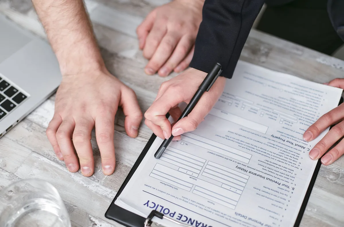 Person signing an insurance policy document with a pen on a wooden desk