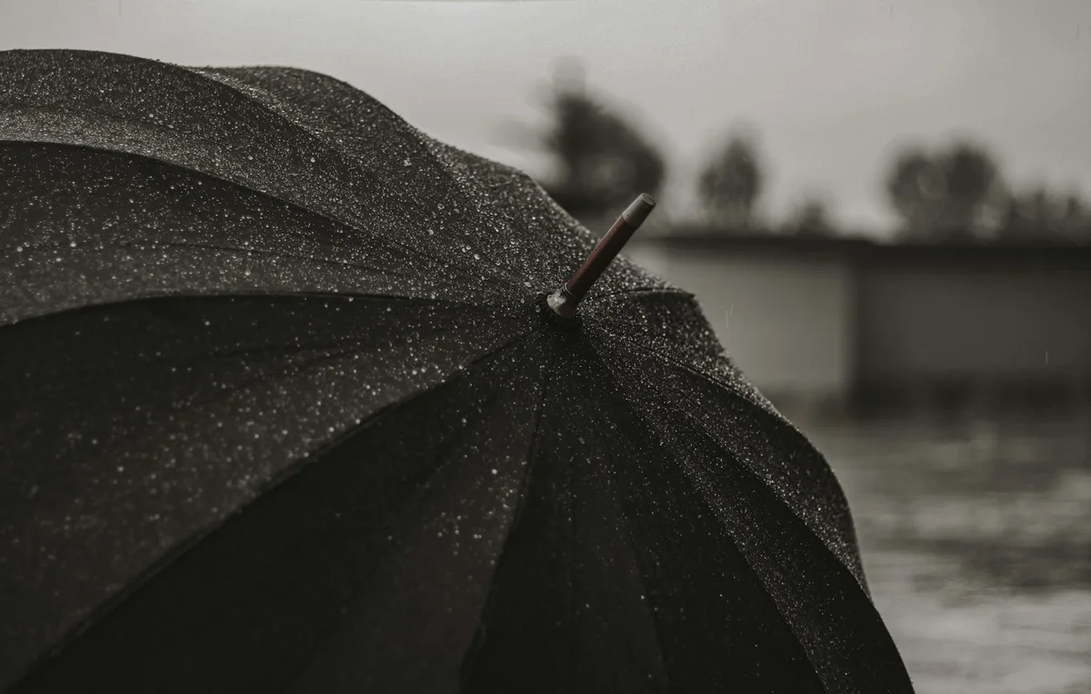 Person holding an open umbrella under rain, representing protection and cover