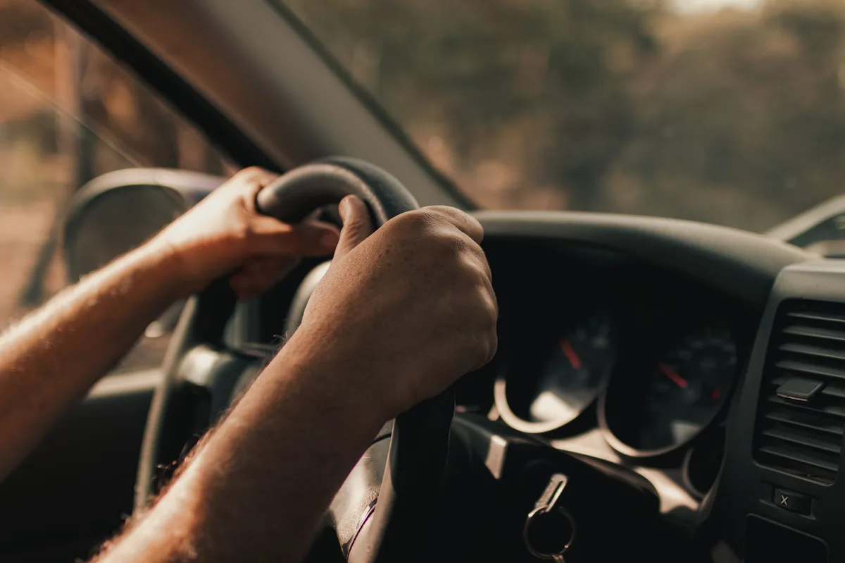 Person driving a car, view from inside the vehicle showing hands on steering wheel