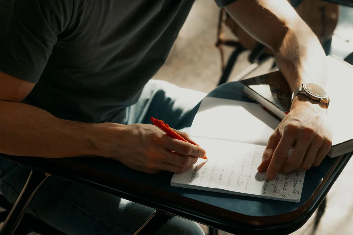 Student writing notes in a notebook with a pen