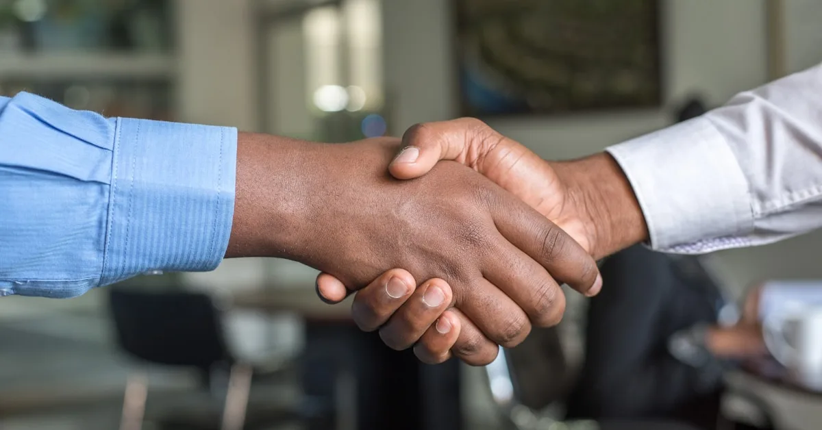 Two business professionals shaking hands in an office setting, representing a business agreement or partnership.